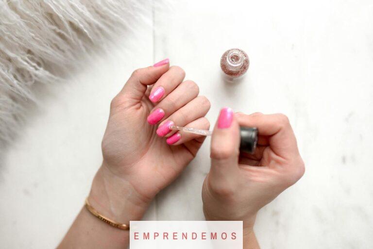 Close-up of a woman applying glitter nail polish to manicured pink fingernails.