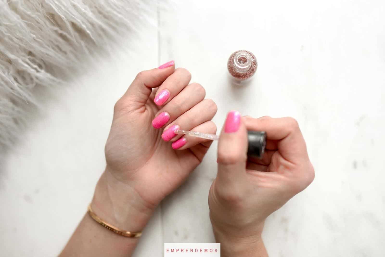 Close-up of a woman applying glitter nail polish to manicured pink fingernails.