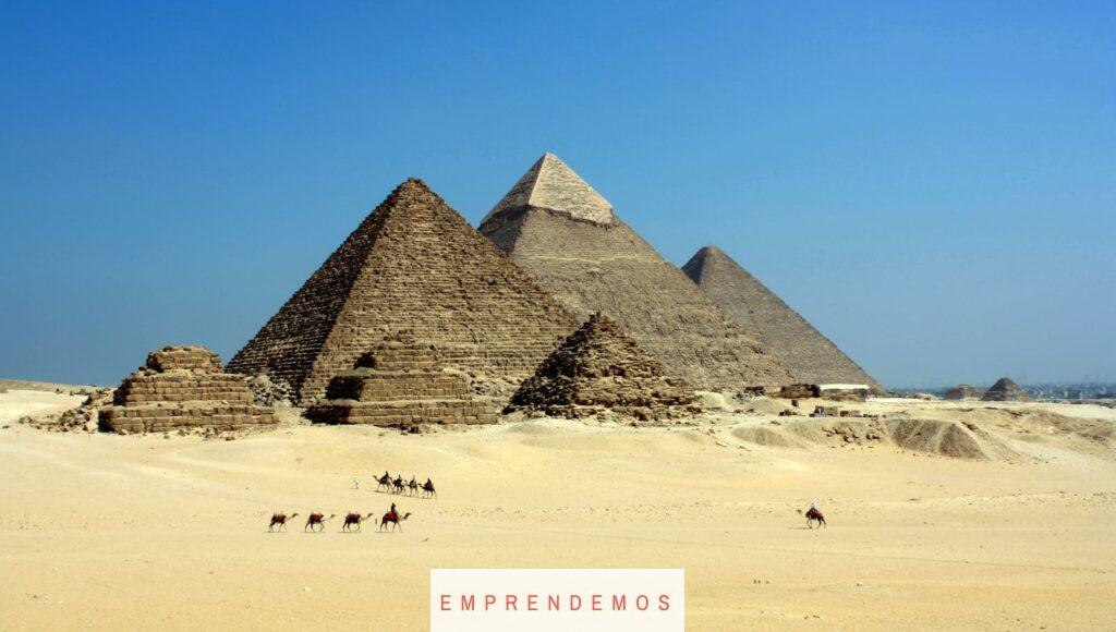 Capture of the iconic Pyramids of Giza under a clear blue sky with camels traversing the sandy desert.