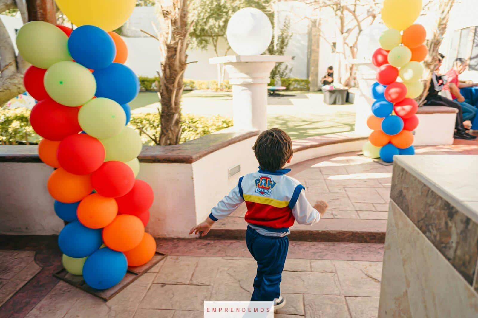 Boy in paw patrol jacket runs past colorful balloons
